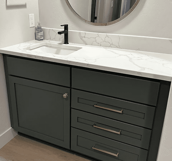 Modern bathroom vanity with dark green cabinets and marble countertop.